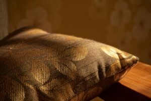 A close-up of a gold-patterned cushion on a wooden surface with warm lighting.